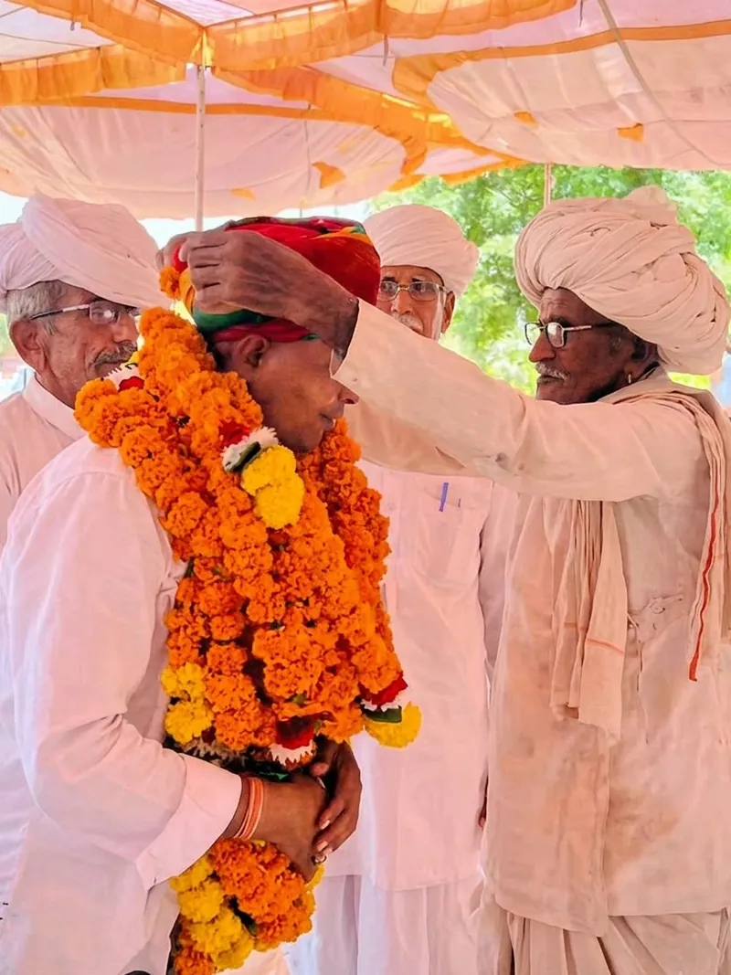 सभा में बुज़ुर्ग साफ़ा बाँधकर आशीर्वाद देते हुए
